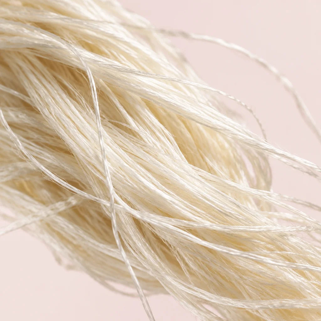 A macro photograph of a small loose bundle of raw ivory silk filaments, their fine uneven strands cr